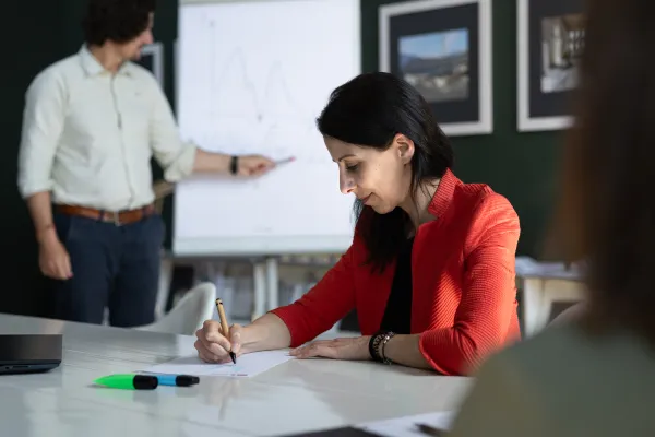 Dozent präsentiert mathematische Funktion an Flipchart, während eine Teilnehmerin aktiv mitschreibt.