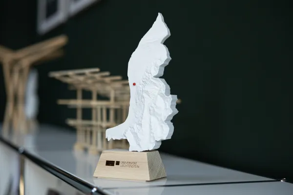 Modell des Fürstentums Liechtenstein mit Universitätslogo im Vordergrund, im Hintergrund Architekturmodelle als Teil einer studentischen Ausstellung.
