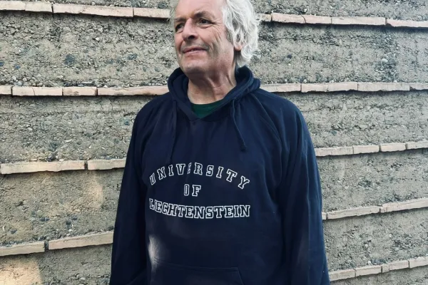 Martin Rauch mit einem Pullover der Universität Liechtenstein vor einer Lehmwand
