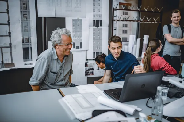 PhD Studierende und Dozierender im Bereich Architektur der Universität Liechtenstein im intensiven Austausch über Entwurfspläne im Architekturstudio.