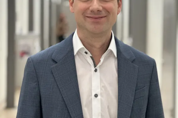 Ein lächelnder Mann in einem blauen Anzug steht in einem modernen, hellen Flur.