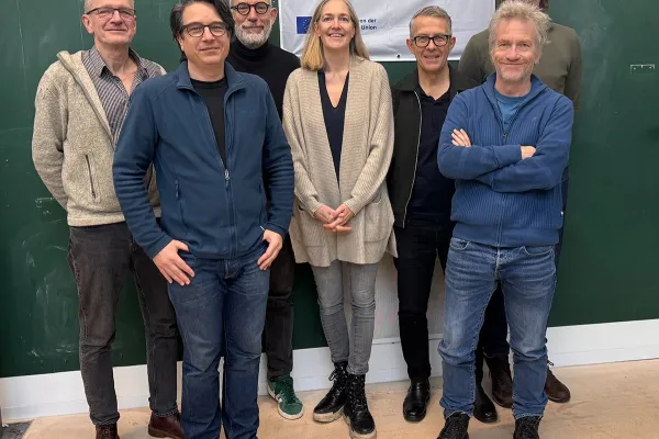 Eine Gruppe von acht Personen steht vor einem grünen Hintergrund. Sie lächeln in die Kamera. Im Hintergrund hängt ein Banner mit der Aufschrift "Erasmus+ Neue Perspektiven, Neue Horizonte".