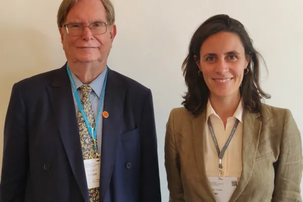 Zwei Personen stehen nebeneinander und lächeln in die Kamera. Beide tragen Namensschilder und sind formell gekleidet.