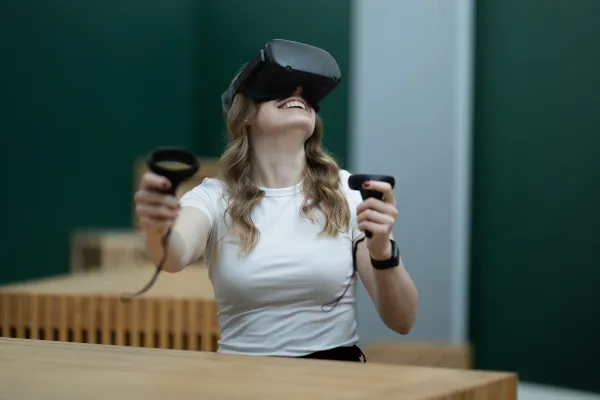 Studentin mit VR-Brille lacht und bewegt Controller im Klassenzimmer.