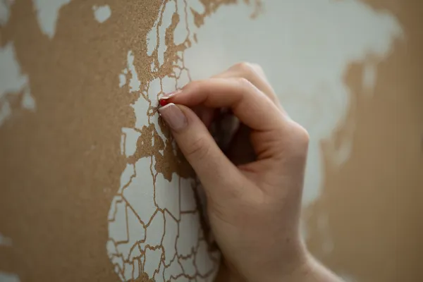 Hand steckt roten Pin in Europakarte zur Markierung eines Ortes.