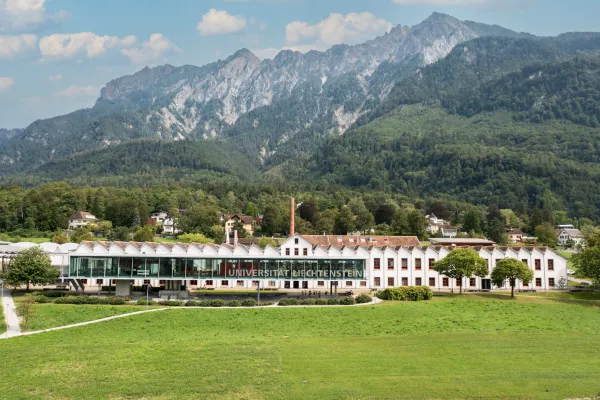 Frontansicht der Universität Liechtenstein mit markanter Glasfassade und grüner Wiese im Vordergrund.