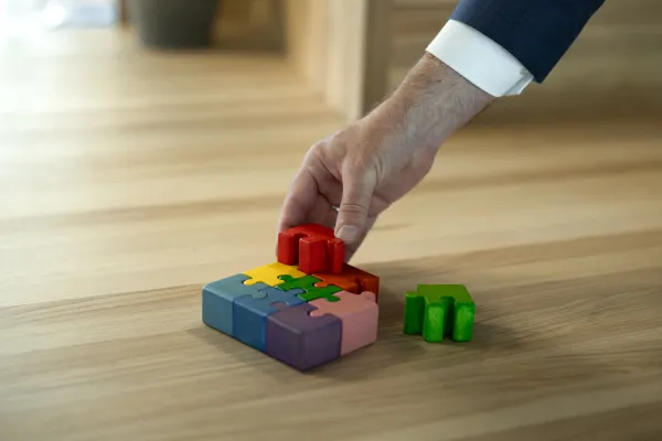 Hand setzt buntes Holzpuzzle auf Holztisch in der Universität Liechtenstein zusammen.