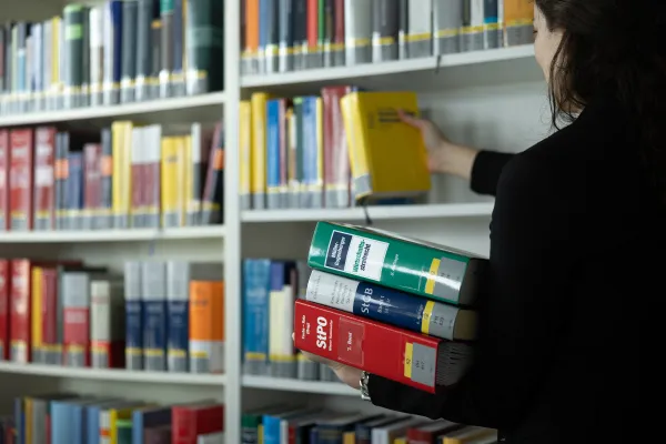 Frau stellt gelbes Fachbuch ins Regal und hält weitere juristische Bücher in der Bibliothek der Universität Liechtenstein.