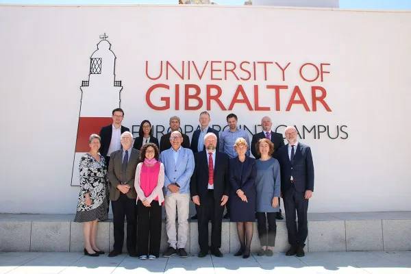 Eine Gruppe von Personen steht vor einem Gebäude mit der Aufschrift "University of Gibraltar". Sie posieren für ein Gruppenfoto bei sonnigem Wetter.