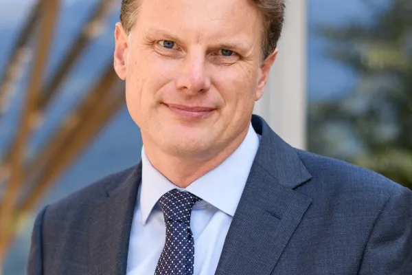 Ein Mann in einem Anzug steht lächelnd vor einem Gebäude.