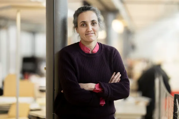 Porträt einer Frau mit schwarzem Pullover, die mit verschränkten Armen an einer Säule lehnt