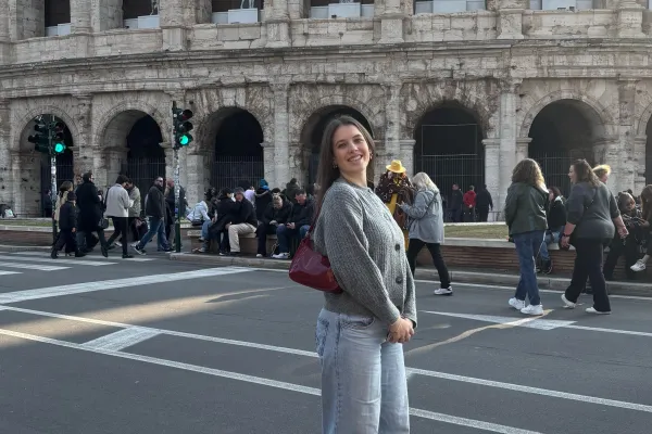 Frau steht lächelnd vor dem Kolosseum, während im Hintergrund Touristen an der Straße entlanggehen.