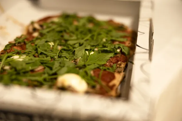 Detailaufnahme einer Pizza mit Rucola und Pilzen in einer geöffneten Pizzaschachtel.